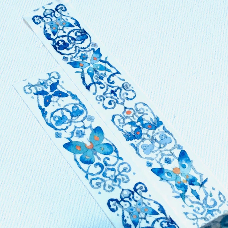 May include: Two rolls of blue and white patterned washi tape with a butterfly design. The tape is on a white background.