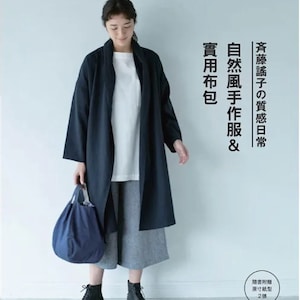 Könnte beinhalten: Eine Frau trägt einen marineblauen Mantel, ein weißes Hemd und eine graue Hose und hält eine blaue Tragetasche. Das Bild enthält japanischen Text. Das Outfit wird durch schwarze Stiefel ergänzt. Das Gesamtthema ist Freizeitkleidung.