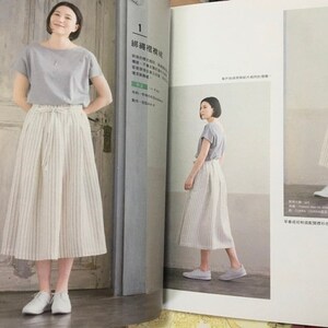 May include: A woman wearing a light gray short-sleeved top and a cream-colored, vertically striped skirt. The skirt is a midi length and has a drawstring waist. She is also wearing white sneakers. The image is from a fashion magazine.