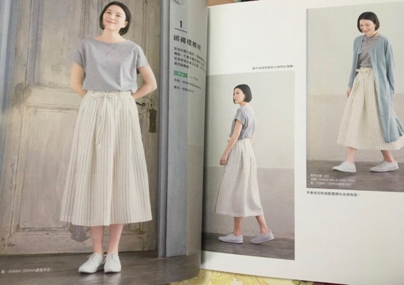 May include: A woman wearing a light gray short-sleeved top and a cream-colored, vertically striped skirt. The skirt is a midi length and has a drawstring waist. She is also wearing white sneakers. The image is from a fashion magazine.