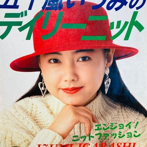 Puede incluir: Una portada de libro con una mujer que lleva un sombrero rojo y un suéter de punto blanco. El título del libro es "Izumi-Igarashi Everyday Knits" y el texto "Enjoy! Knit Fashion" también es visible.
