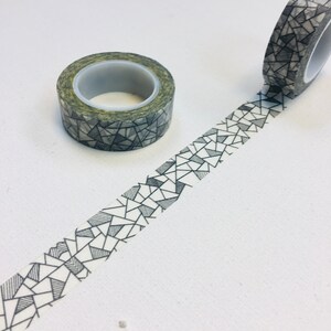 Op de afbeelding: Twee rollen decoratieve washi tape. De tape heeft een geometrisch patroon van zwarte en grijze driehoeken en lijnen op een witte achtergrond. Eén rol is afgerold en toont het patroon dat zich van de rol uitstrekt. De andere rol is intact.