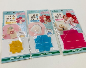 May include: Three Clover brand Tsumami Zaiku flower making plates in yellow, blue, and pink. Each plastic tool is packaged on a card with Japanese text, illustrations of finished fabric flowers, and instructions for creating petal shapes.