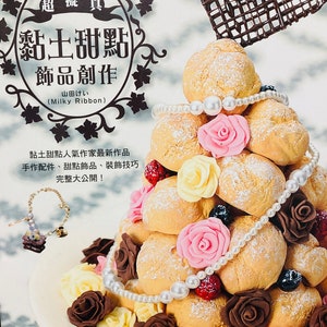 May include: A multi-tiered cake made of cream puffs, decorated with pearl beads, chocolate roses, and pink and yellow fondant roses. The cake is topped with a chocolate heart and the text "超擬真 黏土甜點 飾品創作 山田けい (Milky Ribbon)" in Japanese.