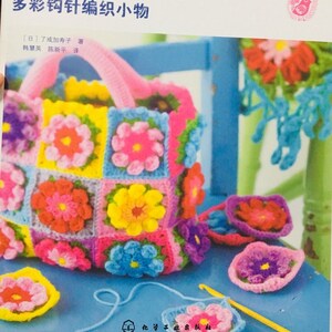 May include: A colorful crocheted bag with a handle, made of squares with flower designs in pink, yellow, blue, and green. The bag is surrounded by smaller crocheted flowers in various colors.