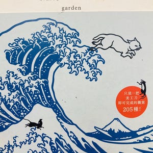 May include: A blue and white papercraft illustration of a Japanese wave with a white cat jumping over it. The image is titled "Floating World Papercraft Collection" and includes the text "Only one craft knife needed to complete 205 designs!"