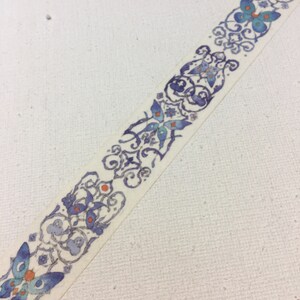 May include: A white washi tape with a repeating pattern of blue and orange butterflies and intricate floral designs.