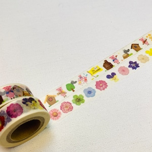 May include: Two rolls of decorative washi tape. One roll shows a repeating pattern of pigs, houses, and flowers. The other roll shows a repeating pattern of flowers and pigs. The text "The Three Little Pigs" is visible on the tape.