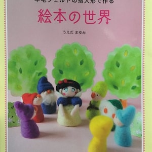 Op de afbeelding: Een boekomslag met de titel "Felt World" in Japanse karakters. De omslag toont een kleurrijke illustratie van viltfiguren uit een sprookje, waaronder Sneeuwwitje, een dwerg en een gele vogel.