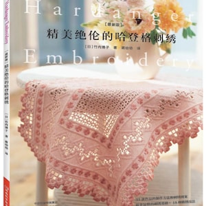 Könnte beinhalten: Ein Buch mit dem Titel "Hardanger Embroidery" mit einem rosa und weißen Blumendesign auf dem Cover. Das Buch zeigt eine Nahaufnahme einer zarten rosa Häkeltischdecke.