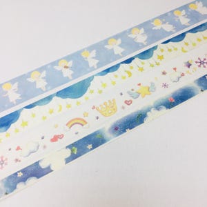 May include: Three rolls of washi tape with a blue and white watercolor background. The top roll features angels with wings, the middle roll has stars, moons, and clouds, and the bottom roll has a starry sky with clouds, flowers, and a rainbow.
