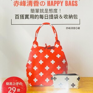 May include: A red tote bag with white plus signs, a smaller cream-coloured pouch with black plus signs, and a book cover with Japanese text. The book is titled "HAPPY BAGS" and features a red circle with Japanese text.