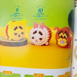 May include: Three colourful bead sprites of Winnie the Pooh, Piglet, and Tigger. The sprites are made with small, round beads in various colours, including yellow, pink, red, brown, and black. The sprites are approximately 5 cm tall. The image includes instructions for making the sprites, with the text "作り方" (Japanese for "how to make") and page numbers.
