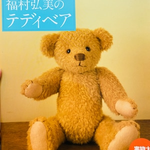 以下が含まれることがあります： 「NHK おしゃれ工房 福田弘美の テディベア」というタイトルの書籍。木製の表面に座っている茶色のテディベアが写っている。本の表紙には、白い文字が書かれた青い長方形がある。