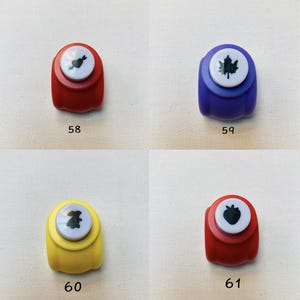 May include: Four plastic craft punches labeled 58, 59, 60, and 61. Number 58 is red with a heart and arrow icon. Number 59 is blue with a maple leaf icon. Number 60 is yellow with a rabbit icon. Number 61 is red with a strawberry icon.