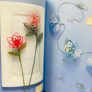May include: A book with two pages showing wire flowers. The left page shows two pink and red flowers on a white background. The right page shows three blue and white flowers on a light blue background. The text "中花" is visible on the right page.