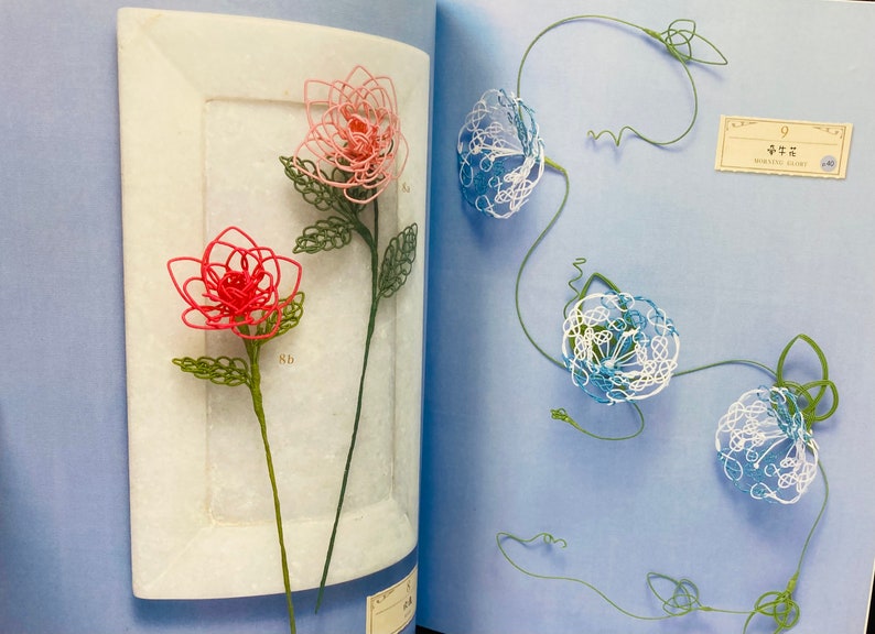 May include: A book with two pages showing wire flowers. The left page shows two pink and red flowers on a white background. The right page shows three blue and white flowers on a light blue background. The text "中花" is visible on the right page.