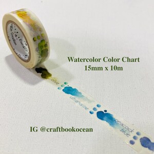Peut inclure: Un rouleau de ruban adhésif washi avec un motif de nuancier aquarelle. Le ruban mesure 1,5 cm de large et 10 m de long. Le motif comprend des éclaboussures d'aquarelle olive, outremer et bleu paon. Le texte "Watercolor Color Chart" est visible.