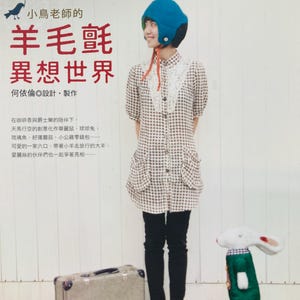 May include: A book cover with a whimsical illustration of a girl wearing a blue helmet and a white shirt with a brown and white checkered pattern. The girl is standing next to a white rabbit wearing a green and red outfit. The book title is "羊毛氈 異想世界" which translates to "Felt World of Fantasy" in English. The book cover also includes the text "小鳥老師的" which translates to "Little Bird Teacher's" in English.