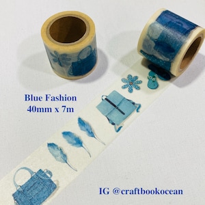 May include: Two rolls of decorative washi tape. One roll is light tan with blue purse designs. The other roll is partially unrolled, revealing a pattern of blue feathers, purses, and a backpack. The text "Blue Fashion 40mm x 7m" is visible.