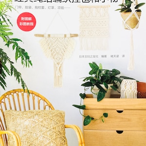 Puede incluir: Un libro titulado "Macramé: Nudos clásicos para tapices de pared y objetos pequeños" con un fondo blanco e imágenes de tapices de pared y colgadores de plantas de macramé. La portada del libro también incluye el texto "附图解 彩图教程" que se traduce como "Con ilustraciones e ilustraciones a color".
