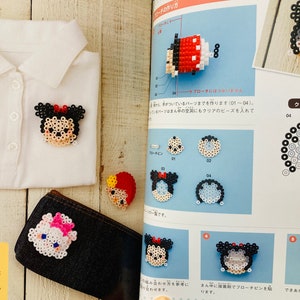 May include: A book with instructions on how to make beaded characters. The book shows a variety of characters, including Mickey Mouse, Minnie Mouse, and other Disney characters. The book also includes a close-up of a beaded character being made.