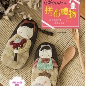 Puede incluir: Dos bolsas de tela con forma de muñeca con caras y detalles bordados. Las bolsas son marrones y beige con un diseño de patchwork. El texto de la portada dice "Shinnie's 拼布禮物 40件為你訂製 的安心十仔 Saienie".