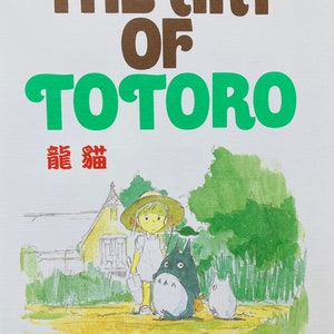 May include: A book cover with the title "THE ART OF TOTORO" in brown and green lettering. The cover features an illustration of a young girl with Totoro and other characters in a field, with a house in the background.