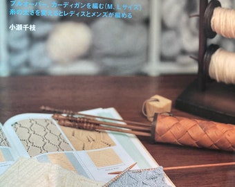 May include: A book titled "More to Know About Knitting: The Art of Knitting" with a white background and a blue title. The book is open to a page showing knitting patterns. There are two knitting needles and a ball of yarn on the page. The book is on a wooden table with a wooden yarn holder and a wooden box.