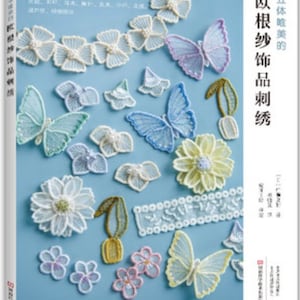 Pode incluir: Uma capa de livro com o título "Motivos de renda bordados" em caracteres japoneses. A capa apresenta uma variedade de delicados motivos de renda, incluindo borboletas, flores e folhas, em cores pastel sobre um fundo azul claro.