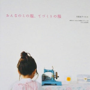 Puede incluir: Una persona joven con el pelo castaño recogido en un moño, lleva un vestido a rayas rosa y blanco, está de pie frente a una máquina de coser vintage. La máquina de coser es azul y tiene una caja de bobina blanca. El texto en la portada del libro dice "おんなのこ の 服, つくり の 服".