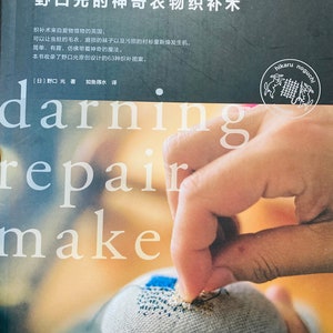 Può includere: Una copertina di libro con il titolo "darning repair make" in testo bianco. La copertina presenta un primo piano di una mano che ripara un tessuto con un ago e filo. Il libro è intitolato "妙手生花 野口光的神奇衣物织补术" in giapponese.