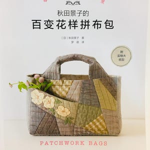 Peut inclure: Un livre intitulé "百变花样拼布包" (One Hundred Variations of Patchwork Bags) par 秋田景子 (Akita Keiko) avec un sac en patchwork sur la couverture. Le sac est fait de différents tissus dans des tons de brun, vert et beige, avec un motif floral sur la poche avant. Le livre est publié par 河南科学技术出版社 (Henan Science and Technology Press).