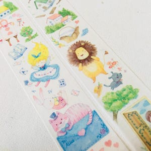 May include: Washi tape with illustrations of Alice in Wonderland characters and scenes. The tape features Alice, a lion, a rabbit, a cat, houses, and playing cards. The tape is white with colourful illustrations.