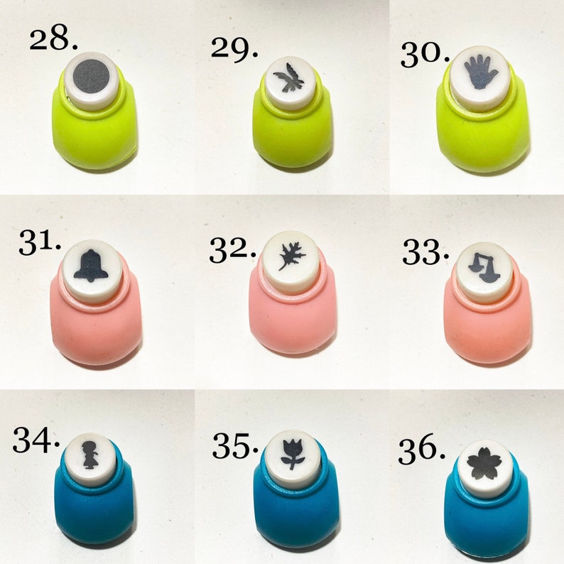 May include: A collection of nine craft paper punches arranged in a grid, numbered 28 through 36. Each punch features a distinct shape on its white top, including a circle, bird, hand, bell, leaf, scales, figure, tulip, and flower in lime, pink, and blue.