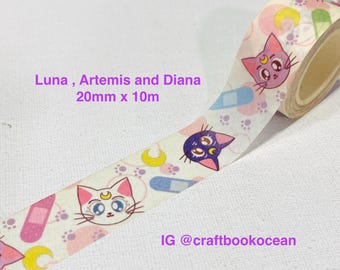 Può includere: Un rotolo di nastro adesivo decorativo washi con un motivo ripetuto di facce di gatto con simboli di luna crescente sulla fronte, impronte di zampe e cerotti. Il testo recita Luna, Artemis and Diana 20mm x 10m e IG @craftbookocean.