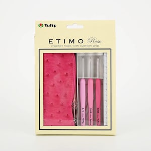 Puede incluir: Un juego de ganchillos Tulip ETIMO Rose con empuñaduras acolchadas en una caja. El juego incluye tres ganchillos rosas, un estuche con cremallera rosa y una regla. La caja tiene el texto "ETIMO Rose" y "crochet hook with cushion grip".