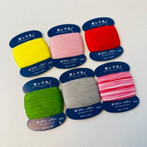 Puede incluir: Seis carretes de hilo para bordar en varios colores, incluyendo amarillo, rosa, rojo, gris, verde y rayas rosa y blancas. Cada carrete está etiquetado con "刺し子糸", que se traduce como "Hilo Sashiko" en inglés. Los carretes tienen todos 40 metros de largo y están hechos en Japón.