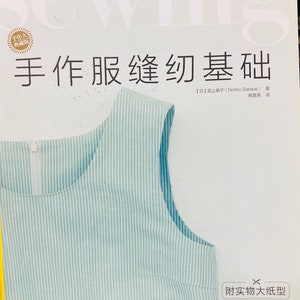 May include: A book cover with the title "Sewing" in large, white letters. The book is about sewing basics and features a blue and white striped fabric sample. The text on the cover is in Japanese and English.