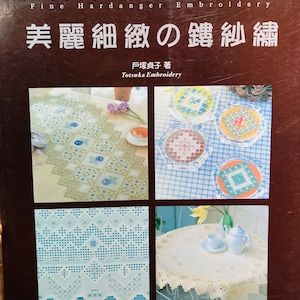 Pode incluir: Um livro intitulado "Fine Hardanger Embroidery" com o texto japonês "美麗細緻の鍵紗繡" e o nome do autor "戶塚貞子 著" (Totsuka Embroidery). A capa do livro apresenta quatro imagens de toalhas de mesa brancas com intrincados desenhos de bordado em azul e branco.