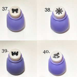 May include: Four purple and white craft paper punches labeled 37, 38, 39, and 40. Each punch features a distinct black icon on the top: a bow, an eight-petaled flower, a butterfly, and a rocking horse, respectively, for paper crafting projects.