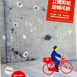 Puede incluir: Un móvil rojo y blanco con un cartero de papel montando una bicicleta roja. El móvil presenta recortes de papel de sobres, corazones, pájaros y una medusa. El título del libro es "Iroken's Mobile Book" y el texto dice "¡Recorta las formas, ata un hilo y luego ensártalas! ¡Un libro sencillo de manualidades de móviles de papel!"