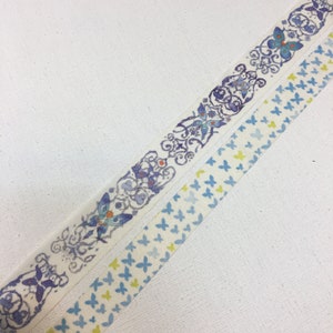 May include: Two rolls of washi tape with butterfly designs. One roll features a repeating pattern of blue butterflies on a white background. The other roll features a more intricate design with blue butterflies, swirls, and floral elements on a white background.
