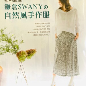 May include: A book cover with a woman wearing a white top and a floral skirt. The book title is "鎌倉SWANYの 自然風手作服" which translates to "Kamakura SWANY's Natural Wind Handmade Clothes". The book cover also includes the text "布料嚴選" which translates to "Fabric Selection".