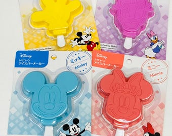 May include: Four silicone popsicle moulds featuring Mickey Mouse, Minnie Mouse, Daisy Duck, and Mickey Mouse's hand. The moulds are packaged on individual cards with the Disney logo and character names.