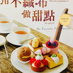 Puede incluir: Portada de libro con el título "My Favorite Felt Sweets!" en inglés y caracteres chinos. La imagen presenta postres de fieltro en un plato blanco, con dos tazas de té y una cuchara. Los postres de fieltro incluyen pasteles, tartas y pasteles.