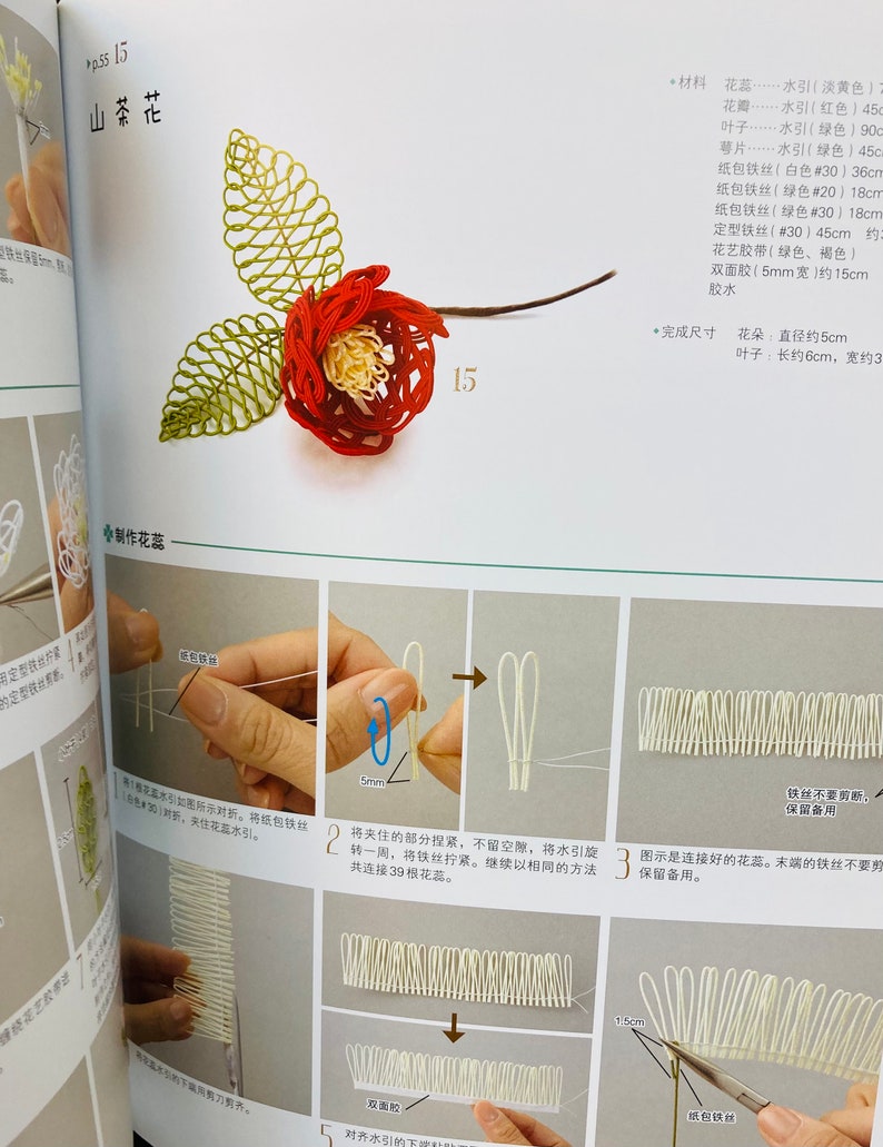 May include: A step-by-step guide to making a camellia flower using white and green string. The instructions show how to create the flower's petals, leaves, and center. The finished flower is approximately 5 cm in diameter.
