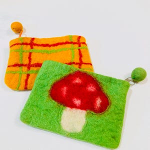 May include: Two felt zipper pouches. One pouch is green with a red and white mushroom design. The other pouch is orange and yellow with a plaid pattern.