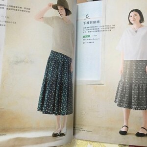 May include: Two women modeling outfits from a fashion magazine. One wears a beige sweater, a patterned skirt, and a hat. The other wears a white top and a patterned skirt. The magazine is open to a page with Japanese text.