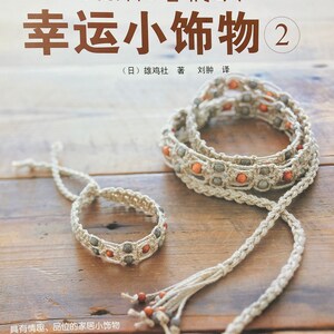 May include: A book titled "Lucky Little Things 2" with a cover featuring a close-up of two bracelets made with natural twine and beads. The bracelets are on a wooden surface. The book cover also features the text "Using Hemp Rope to Weave" in Japanese.